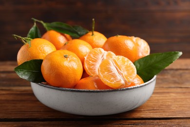Photo of Fresh tangerines with green leaves in bowl on wooden table