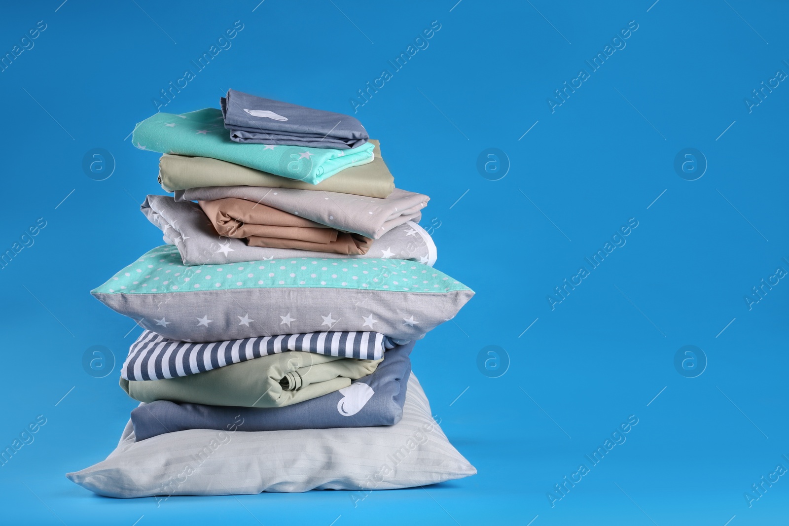 Photo of Stack of clean bed sheets and pillows on blue background. Space for text