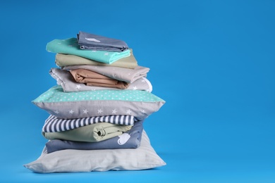 Stack of clean bed sheets and pillows on blue background. Space for text