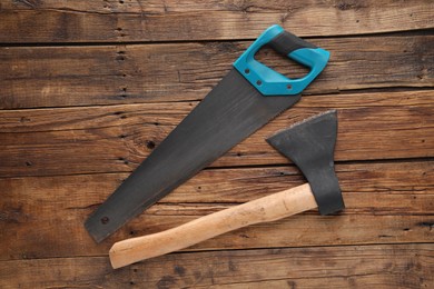 Saw with light blue handle and axe on wooden background, flat lay