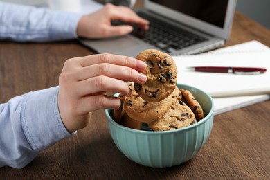 Photo of Office worker taking chocolate chip cookie from bowl at workplace, closeup