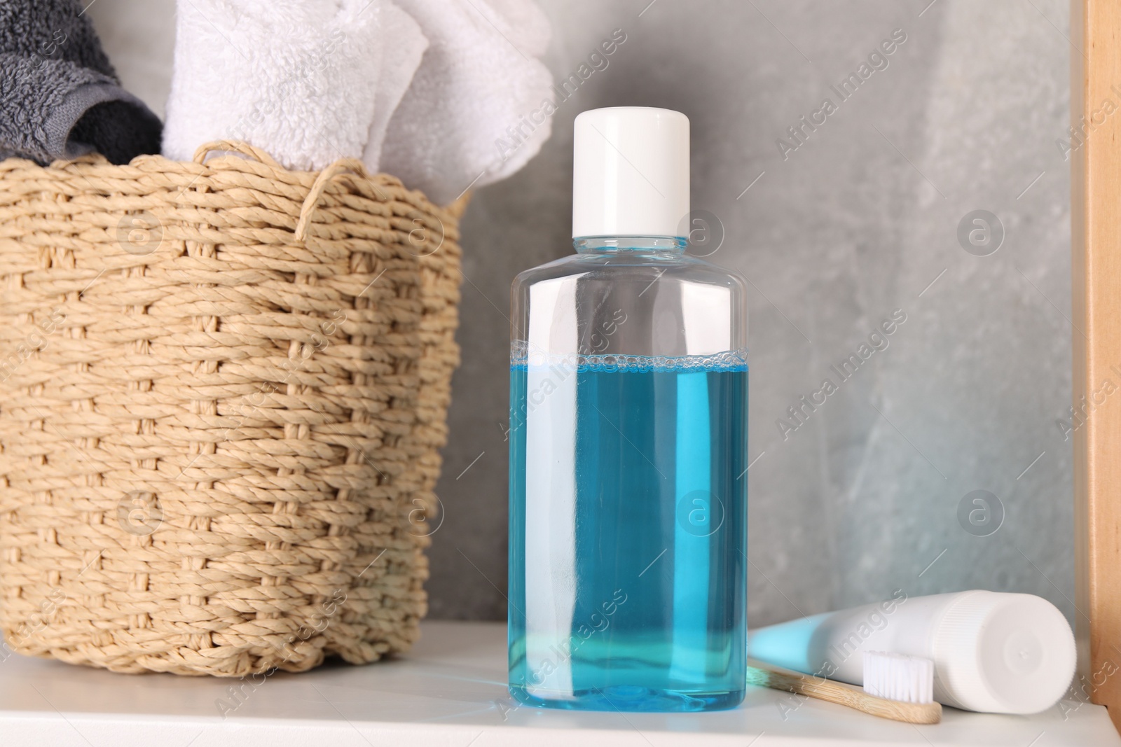 Photo of Bottle of mouthwash, toothpaste, toothbrush and towels on shelf in bathroom