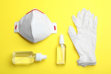 Photo of Medical gloves, respiratory mask and hand sanitizers on yellow background, flat lay