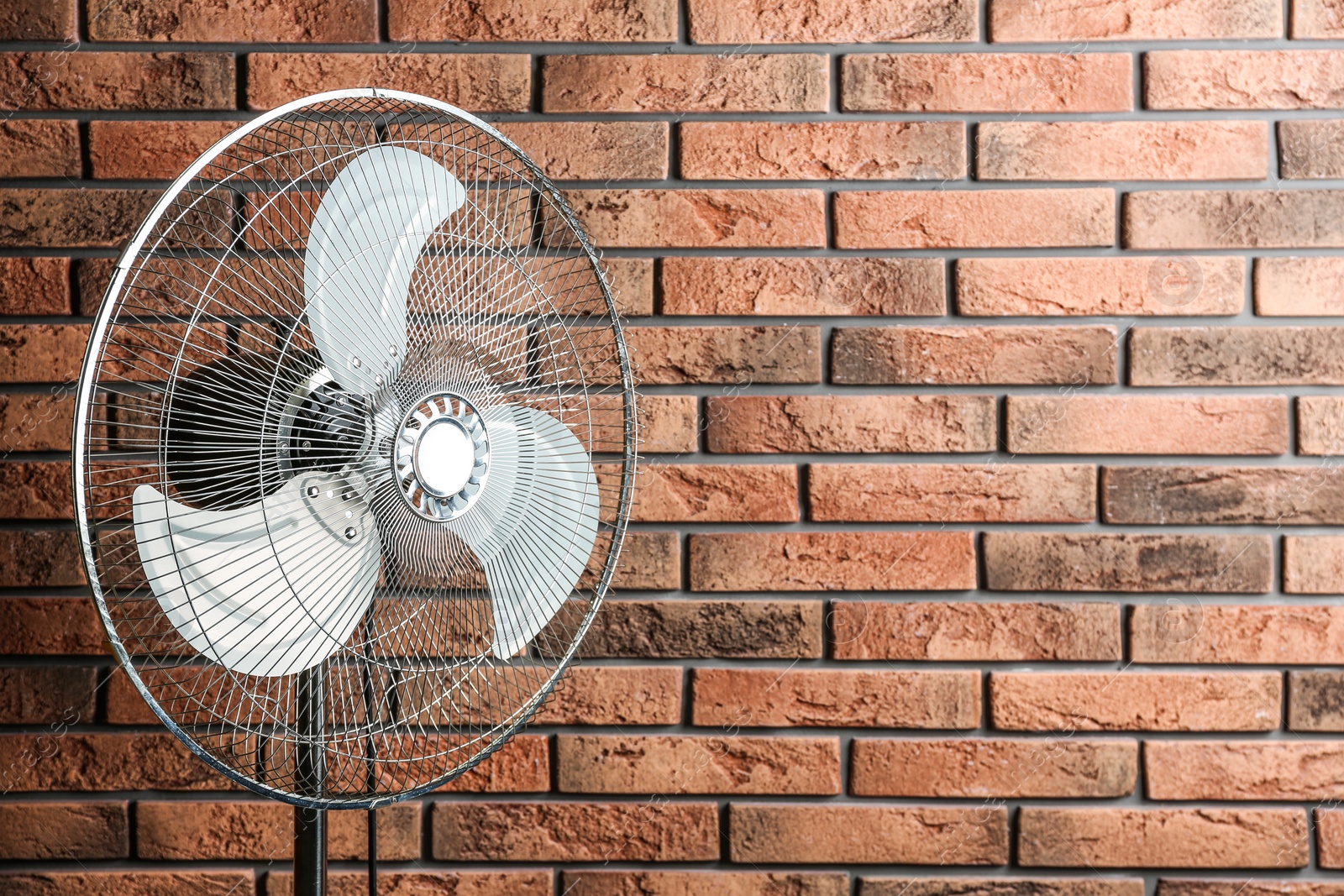 Photo of Electric fan near brick wall, space for text. Summer heat