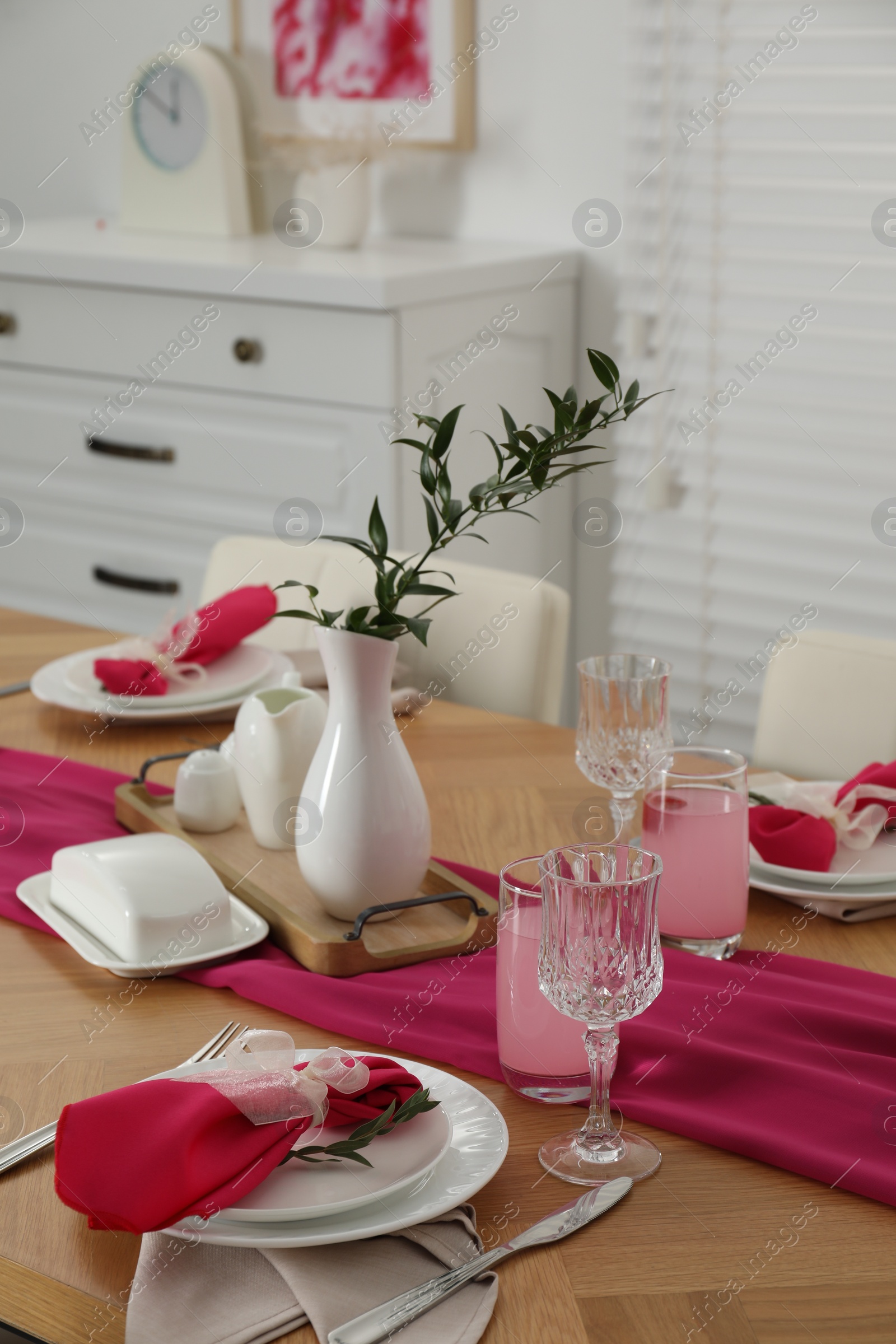 Photo of Color accent table setting. Glasses, plates, pink napkins and vase with green branch in dining room