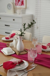 Photo of Color accent table setting. Glasses, plates, pink napkins and vase with green branch in dining room