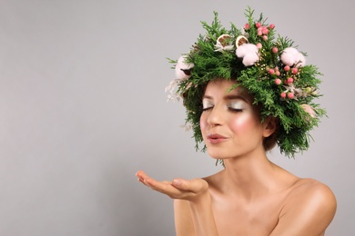 Young woman wearing wreath on grey background