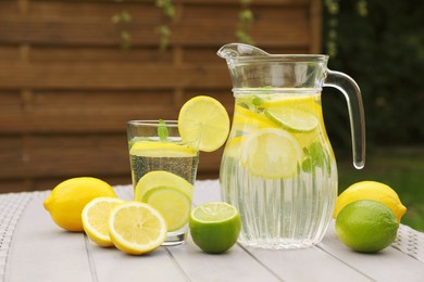 Water with lemons and limes on white wooden table outdoors