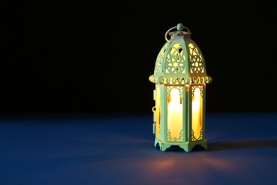 Photo of Decorative Arabic lantern on table against dark background. Space for text