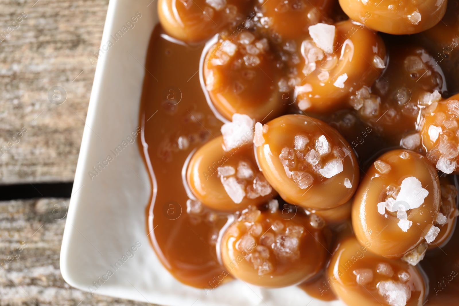Photo of Tasty candies, caramel sauce and salt on wooden table, top view