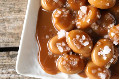 Tasty candies, caramel sauce and salt on wooden table, top view