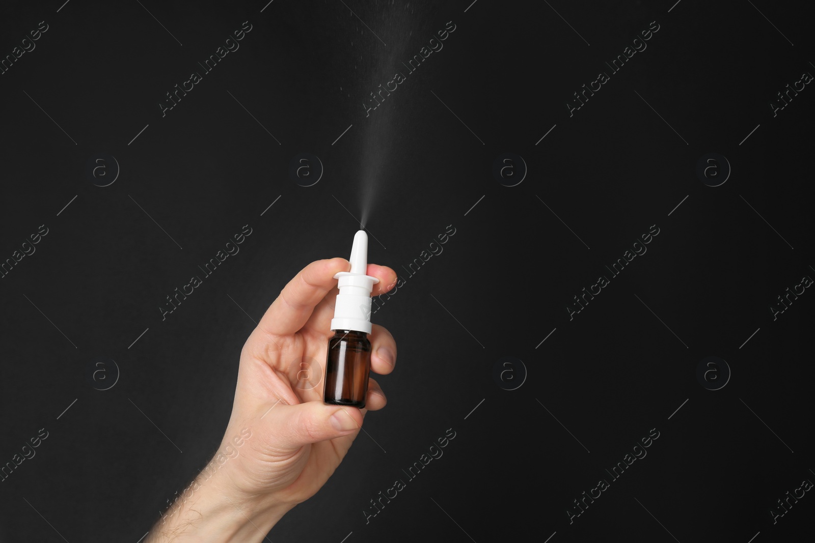 Photo of Nasal congestion. Man spraying remedy from bottle on black background, closeup with space for text