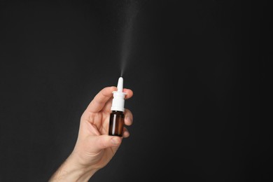 Nasal congestion. Man spraying remedy from bottle on black background, closeup with space for text