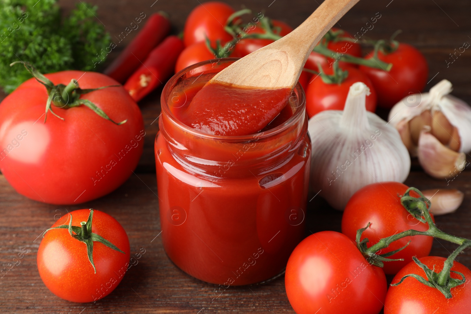 Photo of Taking tasty ketchup with spoon from jar on wooden table, closeup