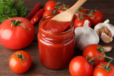 Photo of Taking tasty ketchup with spoon from jar on wooden table, closeup