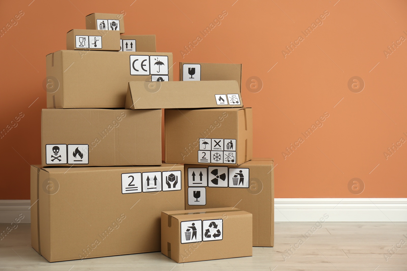 Photo of Cardboard boxes with different packaging symbols on floor near orange wall. Parcel delivery