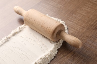 Photo of Flour and rolling pin on wooden table, closeup