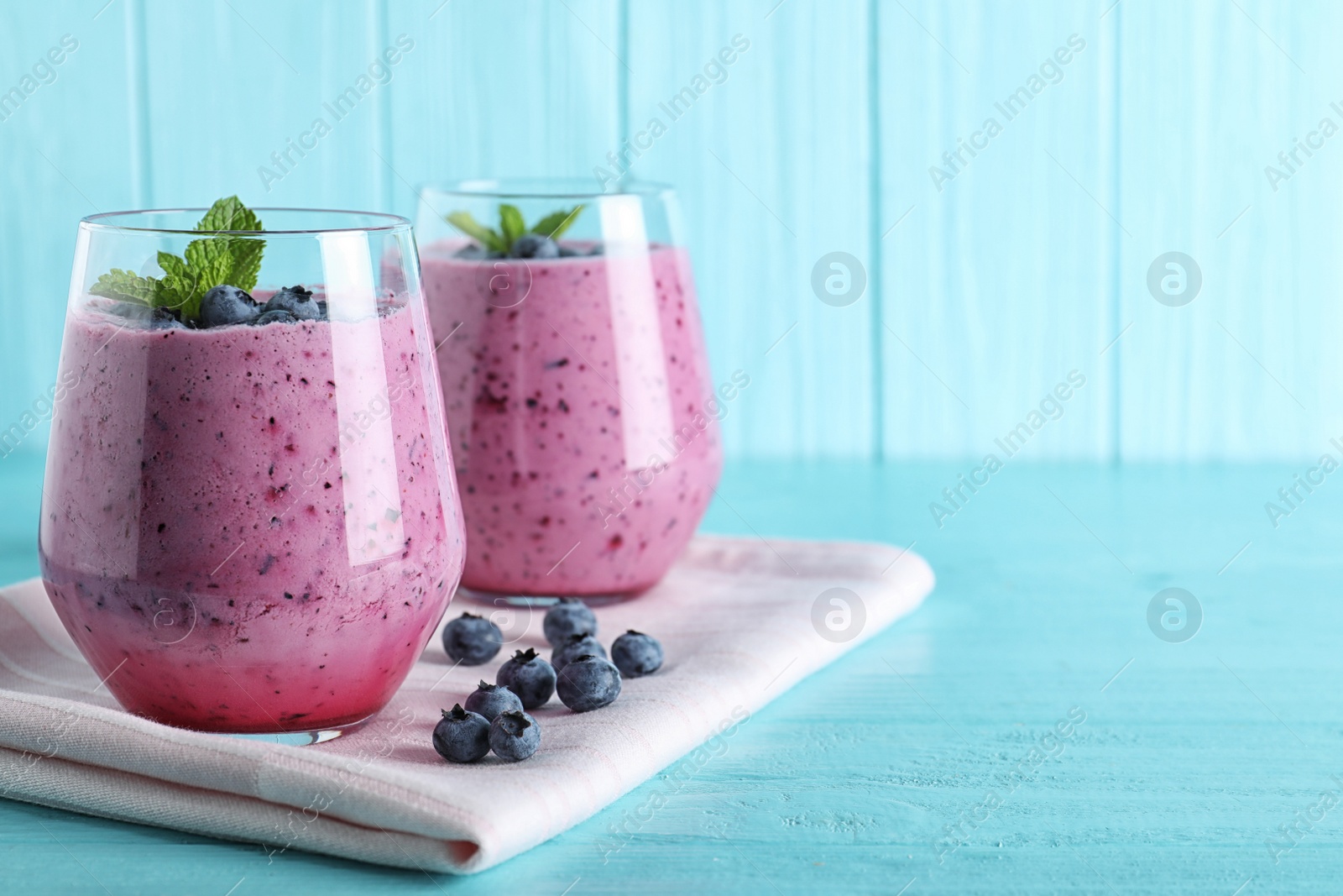 Photo of Glasses of tasty blueberry smoothie and fabric on light blue wooden table, space for text