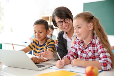 Photo of Female teacher helping children with assignment at school