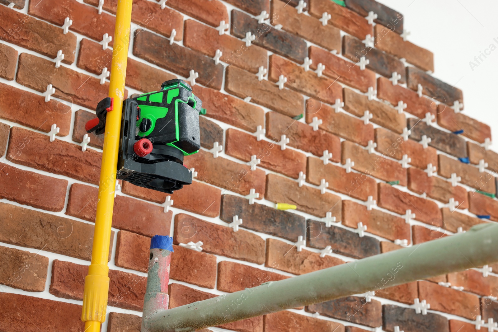 Photo of Modern cross line laser level near wall indoors, space for text. Tiles installation process