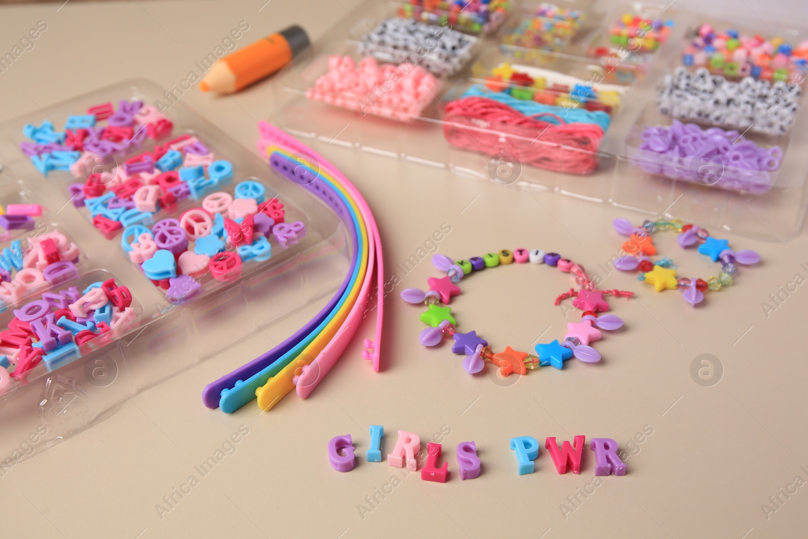 Photo of Handmade jewelry kit for kids. Colorful beads, wristbands and bracelets on beige background, closeup