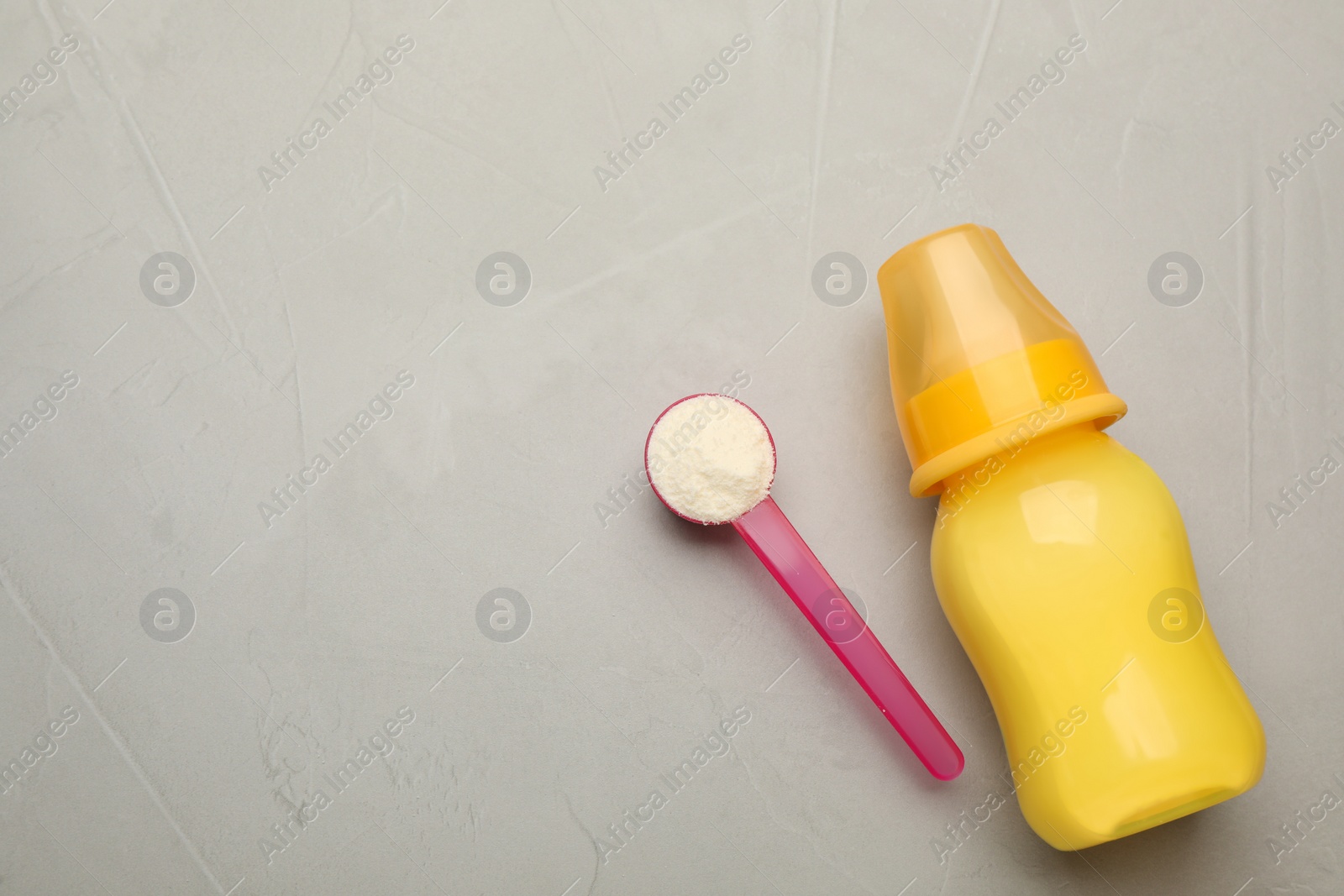 Photo of Feeding bottle with infant formula, scoop of powder and space for text on grey table, flat lay. Baby milk