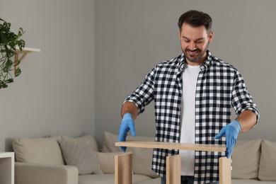 Man assembling wooden furniture in living room. Space for text