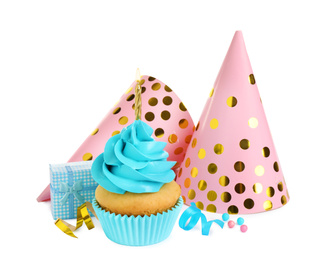 Photo of Delicious birthday cupcake with candle, gift and party caps on white background