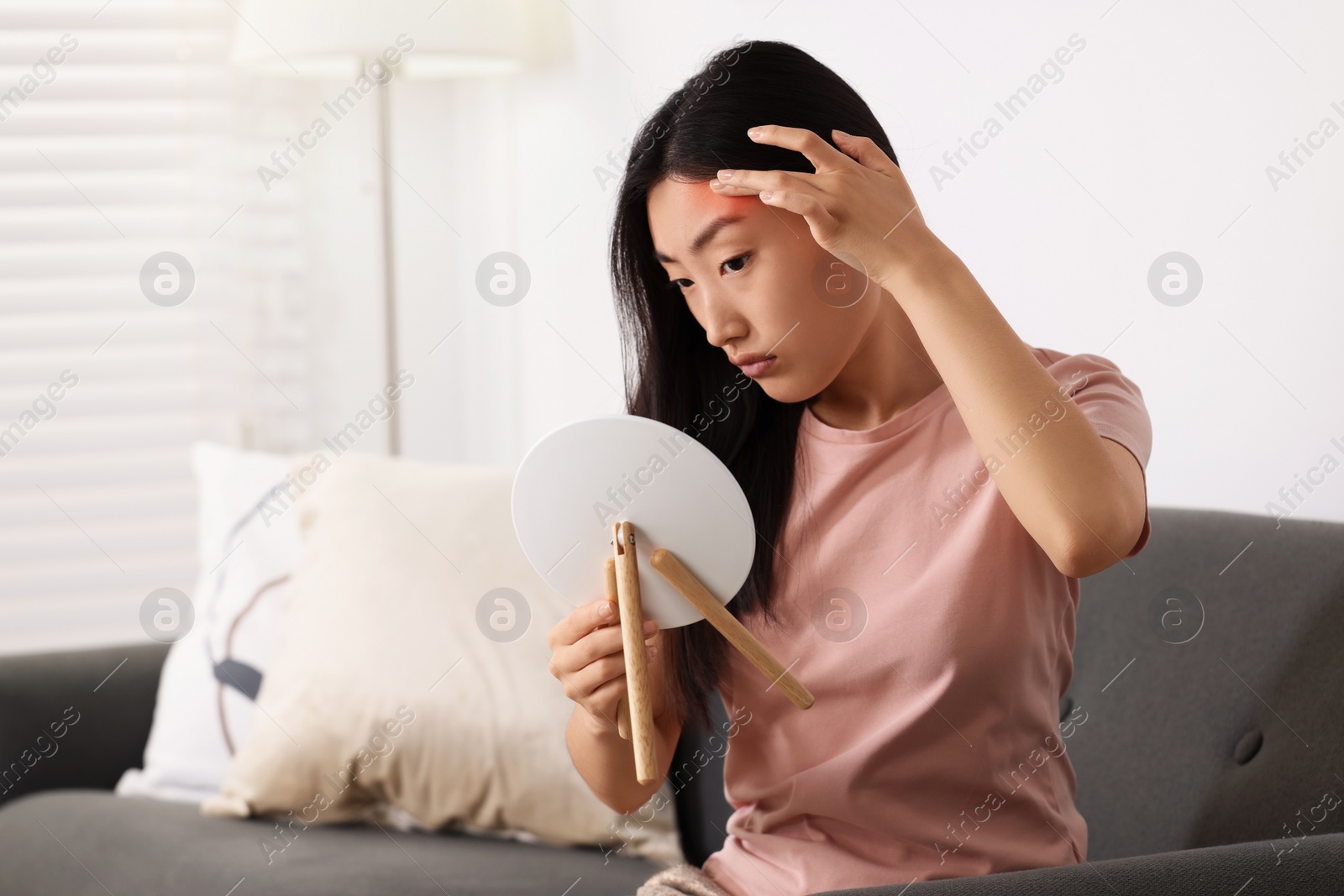 Photo of Suffering from allergy. Young woman with mirror checking her face in living room