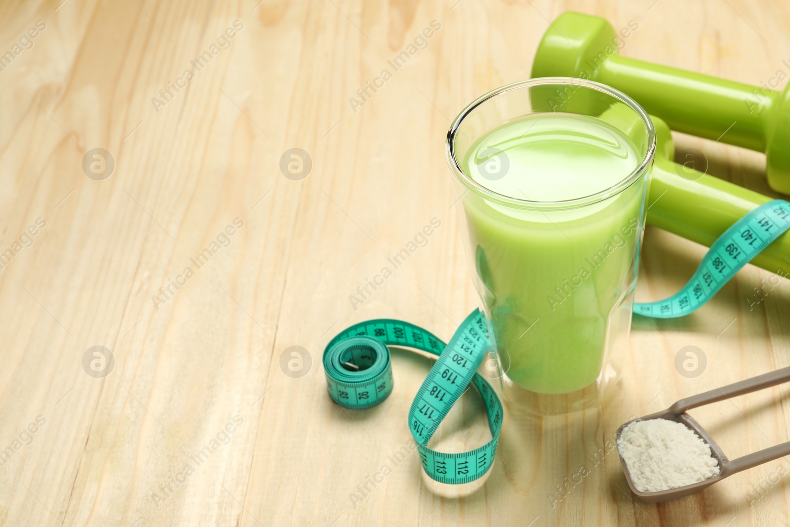 Photo of Tasty shake, dumbbells, measuring tape and powder on wooden table, space for text. Weight loss