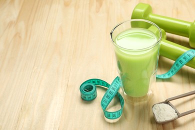 Photo of Tasty shake, dumbbells, measuring tape and powder on wooden table, space for text. Weight loss