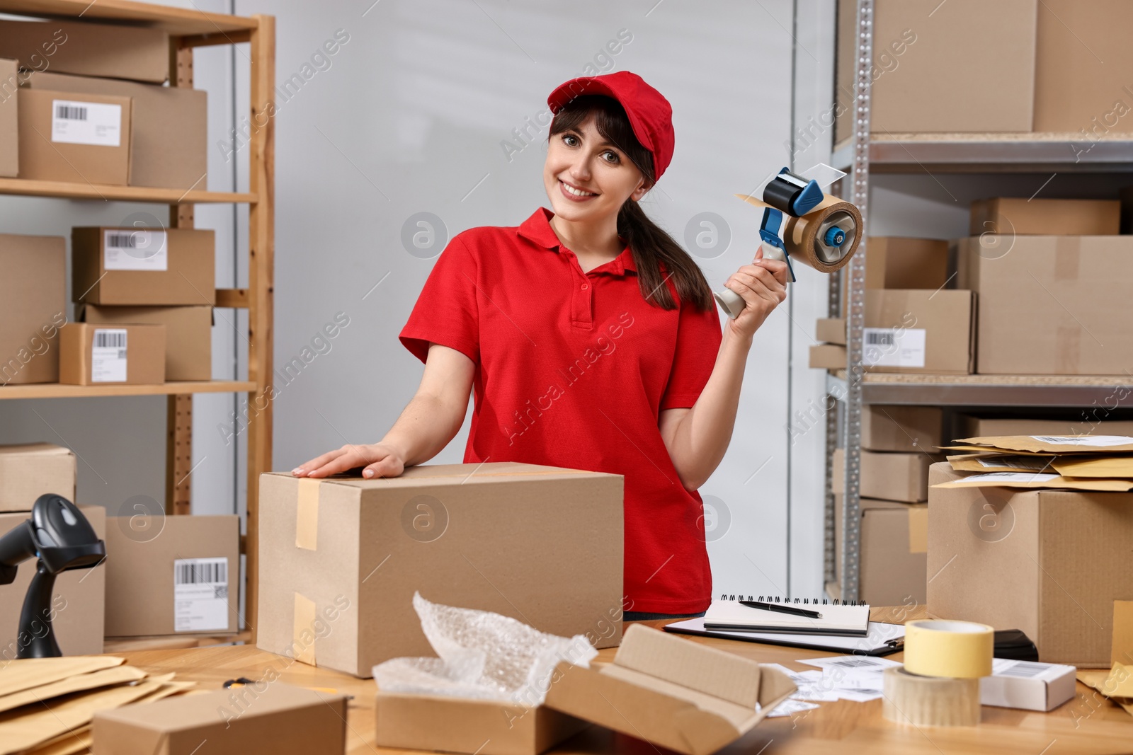 Photo of Parcel packing. Post office worker with tape dispenser and box at wooden table indoors