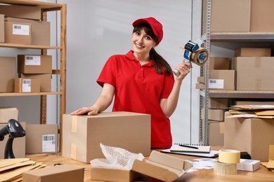 Photo of Parcel packing. Post office worker with tape dispenser and box at wooden table indoors