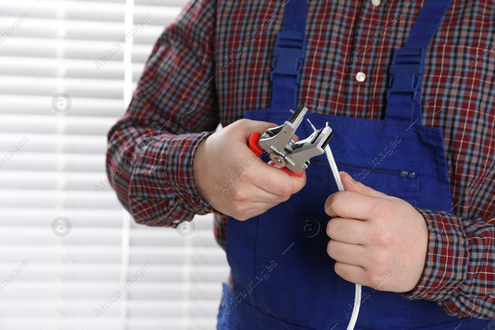 Photo of Professional electrician in uniform stripping wiring indoors, closeup