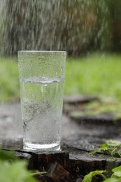 Photo of Splashing out water into glass on wooden stump in green grass outdoors