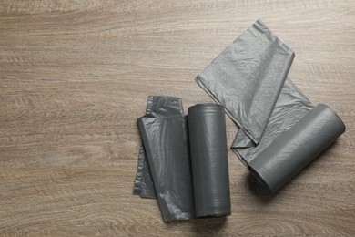 Photo of Rolls of grey garbage bags on wooden table, flat lay. Space for text