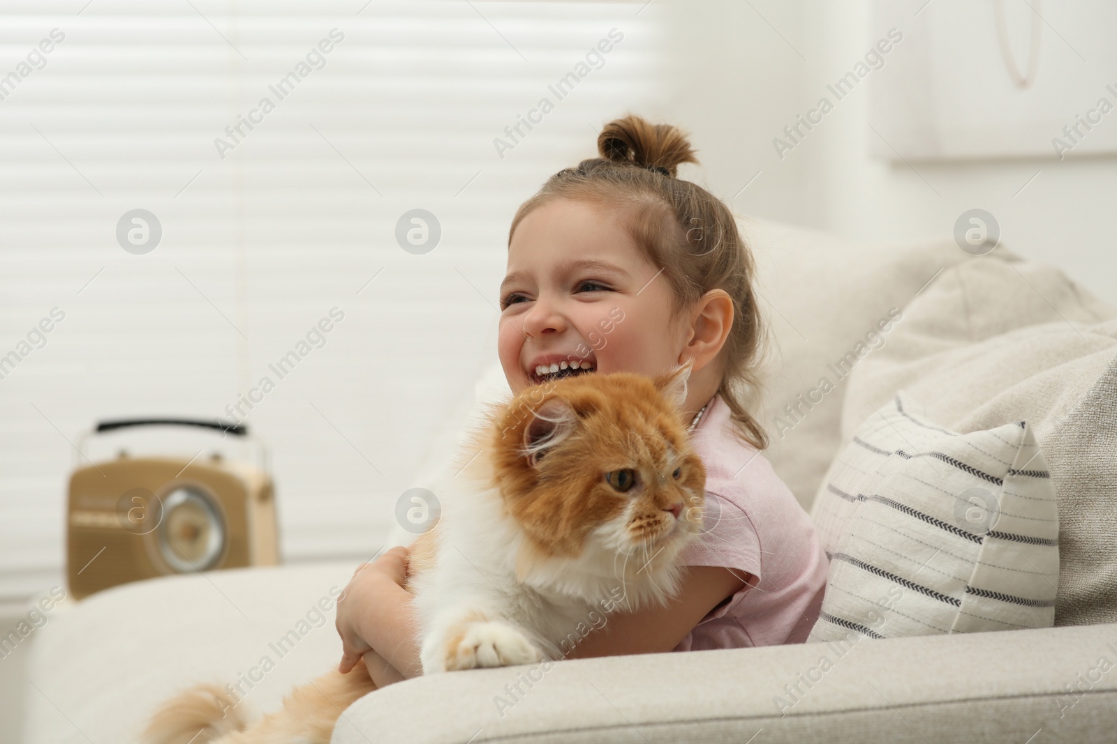 Photo of Happy little girl hugging cute cat on sofa at home