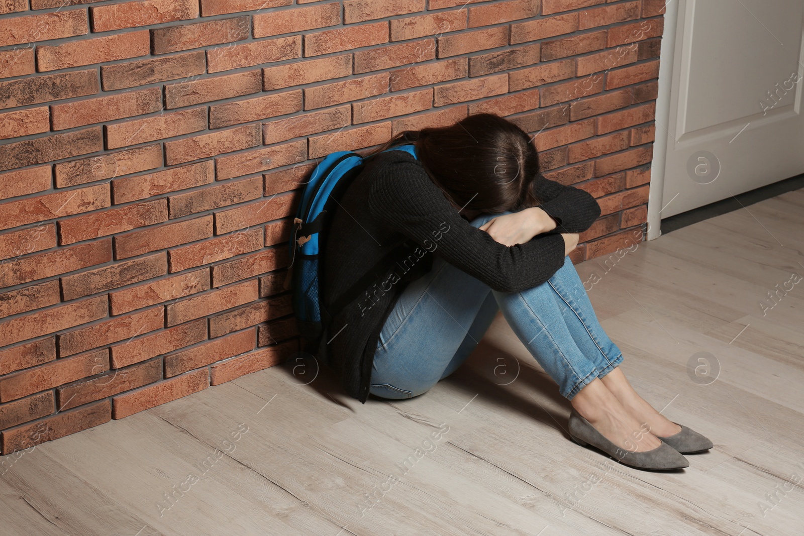 Photo of Upset teenage girl with backpack sitting on floor near wall. Space for text