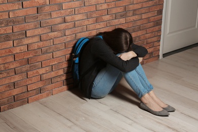 Upset teenage girl with backpack sitting on floor near wall. Space for text