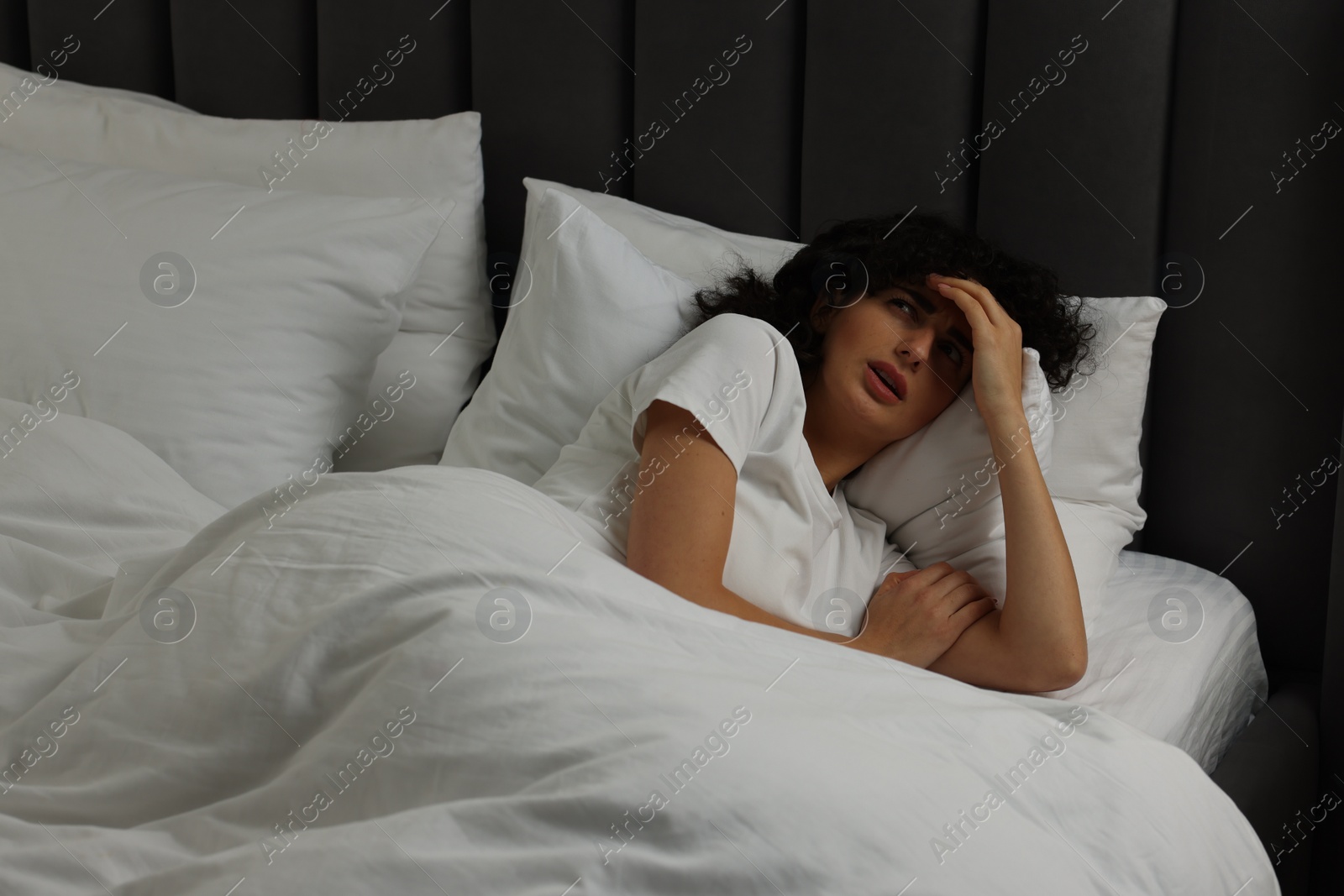 Photo of Young woman suffering from headache in bed at night