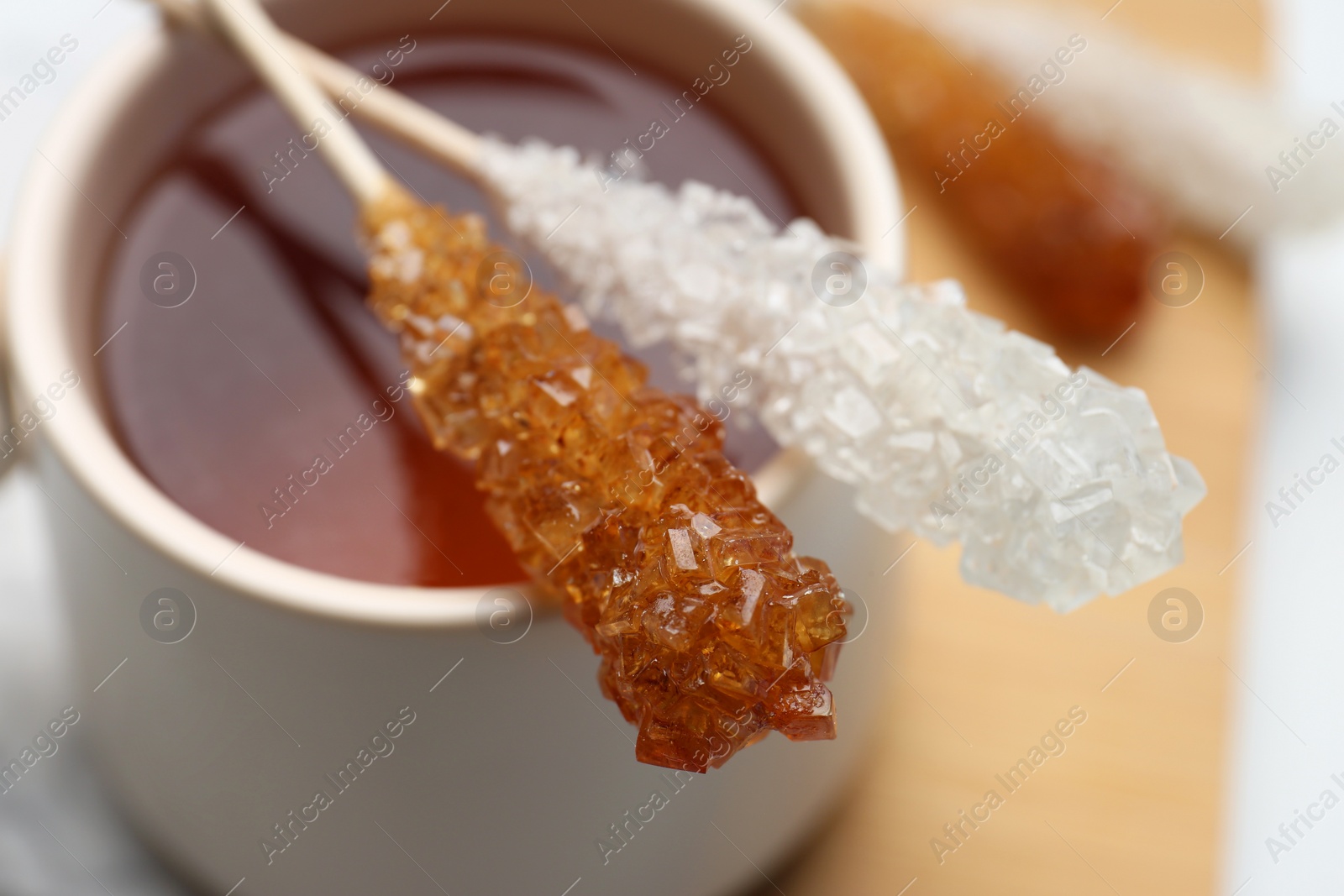 Photo of Sticks with sugar crystals and cup of tea on table, closeup