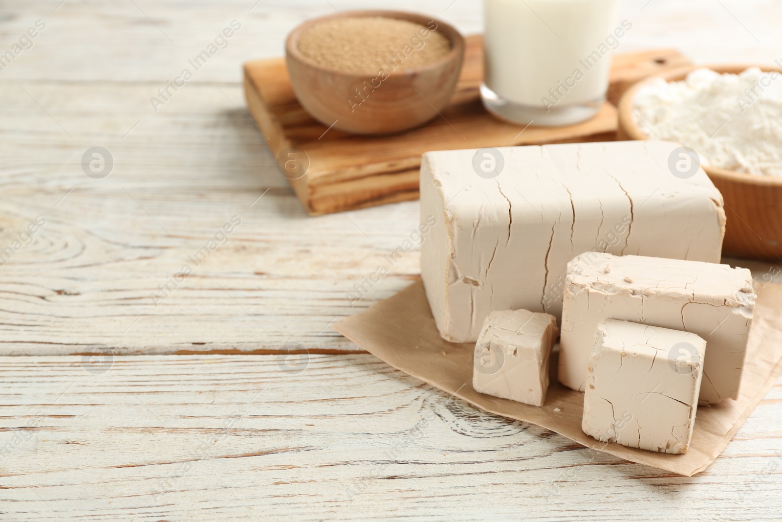 Photo of Pieces of compressed yeast on white wooden table. Space for text