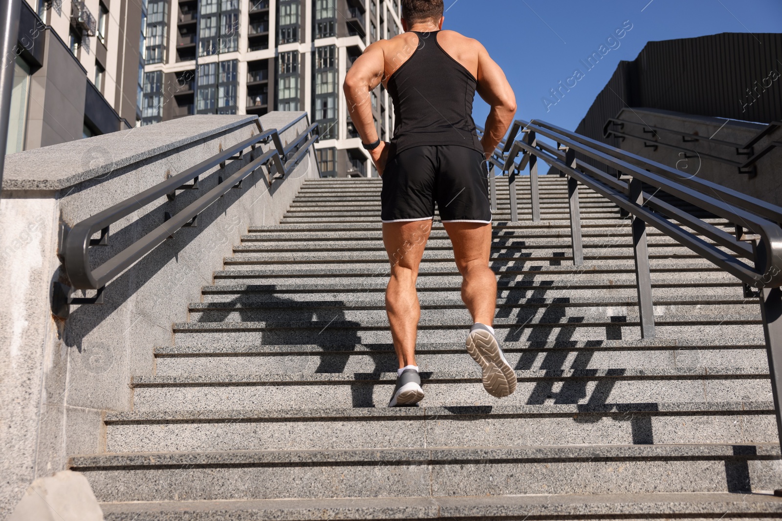 Photo of Man running up stairs outdoors on sunny day, back view