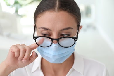 Photo of Woman wiping foggy glasses caused by wearing medical mask indoors, closeup