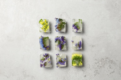Photo of Ice cubes with flowers on light stone background, flat lay