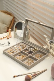 Photo of Elegant jewelry box with beautiful bijouterie and makeup products on dressing table indoors