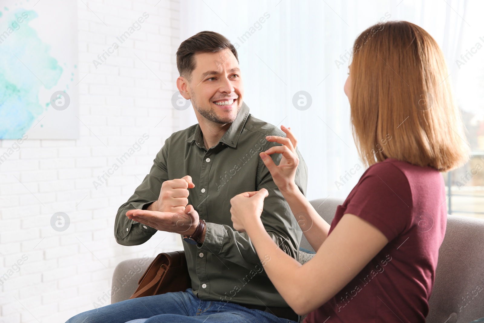 Photo of Hearing impaired friends using sign language for communication on sofa in living room