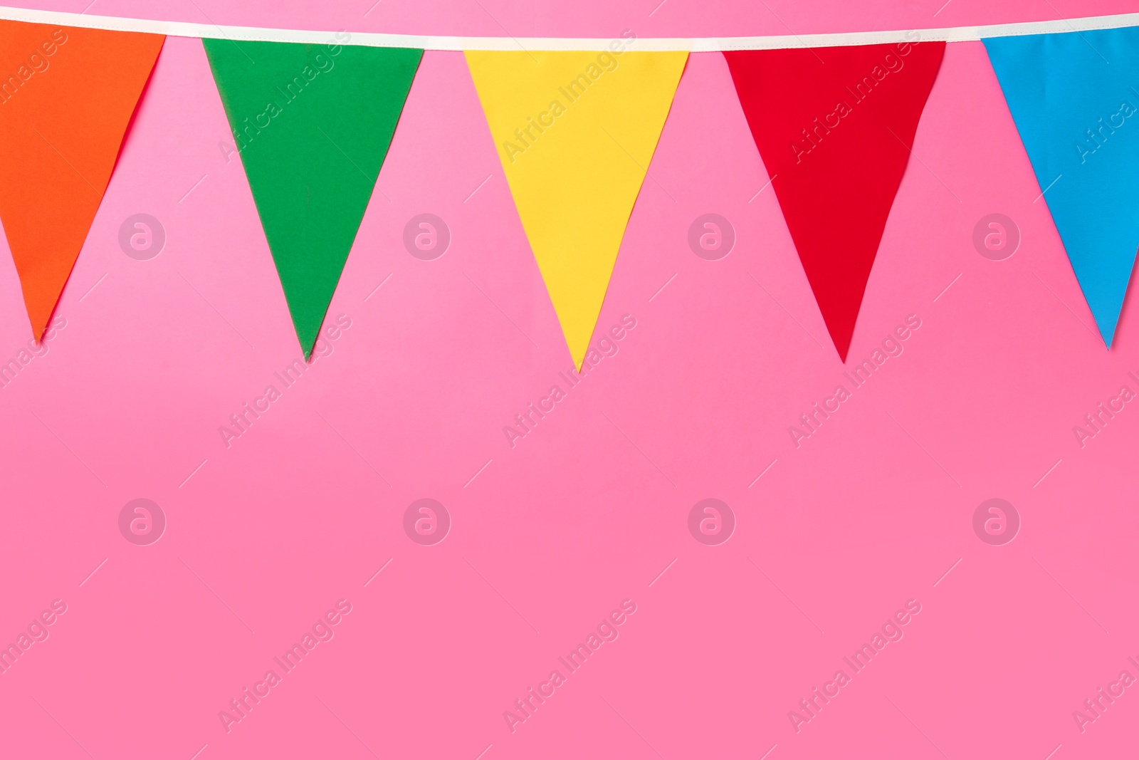 Photo of Bunting with colorful triangular flags on pink background. Space for text