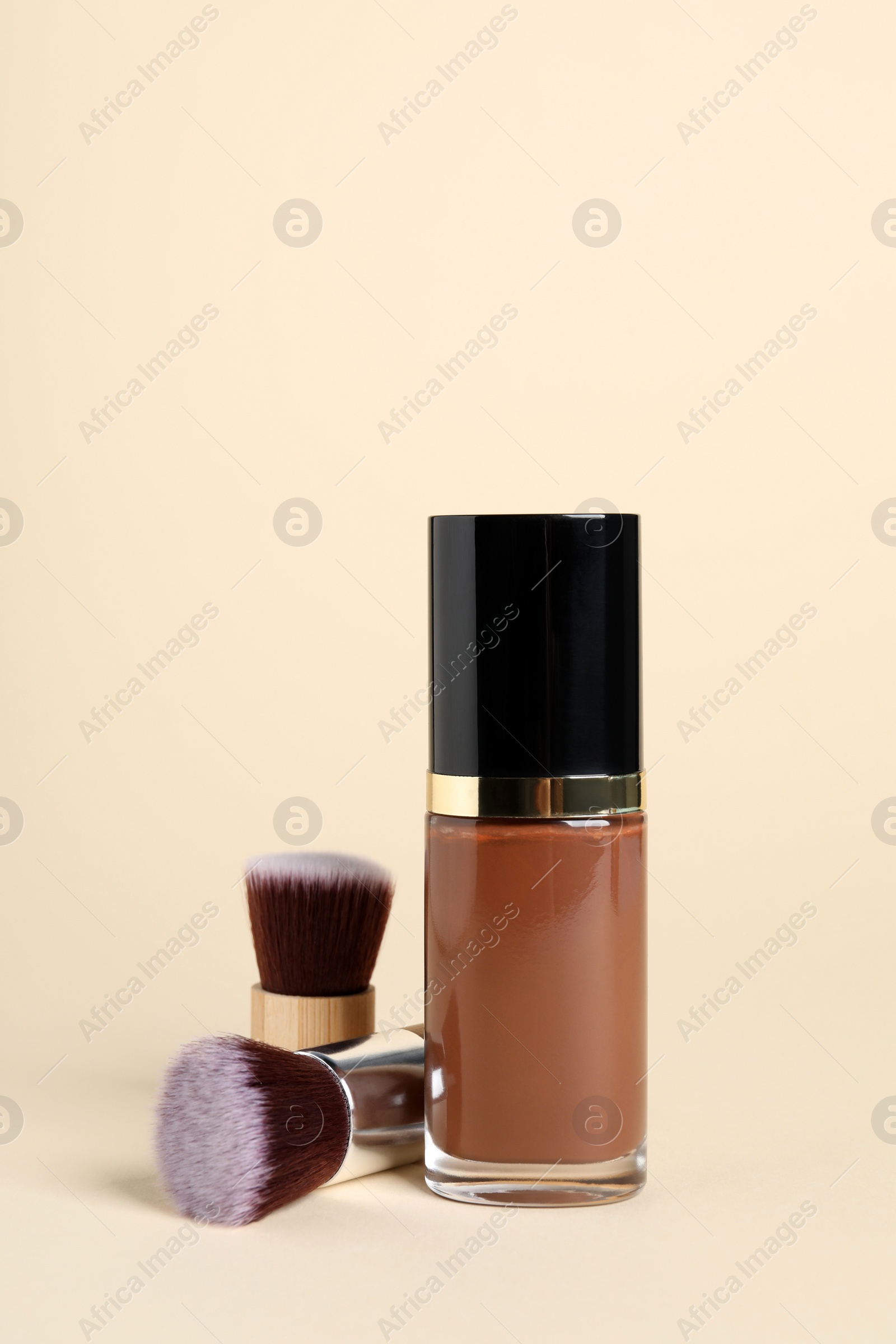 Photo of Bottle of skin foundation and brushes on beige background. Makeup product