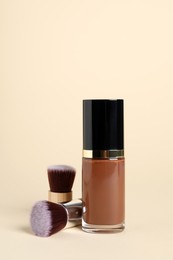 Bottle of skin foundation and brushes on beige background. Makeup product